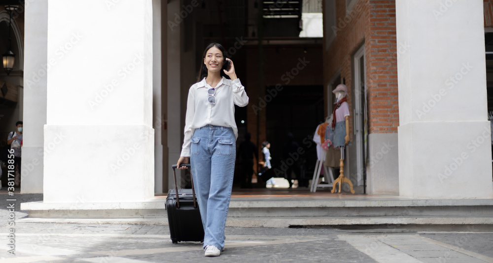 Asian woman holds a travel bag preparing to go to the accommodation and chat on the phone to a friend to meet up for a holiday party, Trolley bag, Long weekend travel, Tourism festival concept. Asian woman holds a travel bag preparing to go to the accommodation and chat on the phone to a friend to meet up for a holiday party, Trolley bag, Long weekend travel, Tourism festival concept.