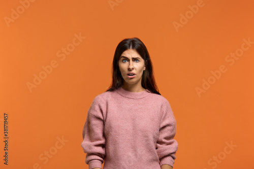 Are you serious. Portrait of shocked stunned beautiful woman in pink sweater, looking dissatisfied and surprised. On orange background © 5M