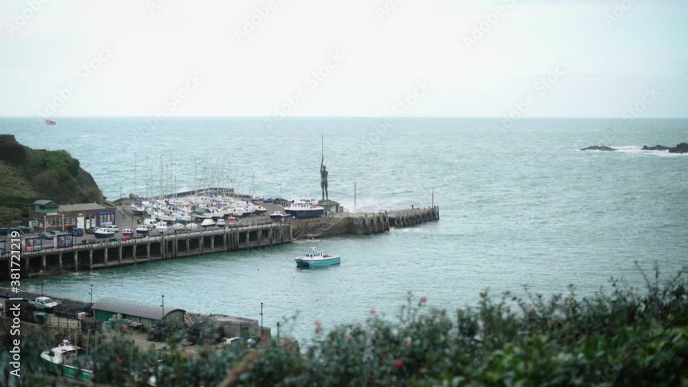 Boats Arriving At The Ilfracombe Harbour With The Verity Statue Against The Calm Sea At Ilfracombe, North Devon Coast, England, United Kingdom. - wide shot Boats Arriving At The Ilfracombe Harbour With The Verity Statue Against The Calm Sea At Ilfracombe, North Devon Coast, England, United Kingdom. - wide shot