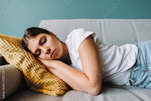 Fotografie Young caucasian woman lying on sofa in living room sleeping after hard-working d