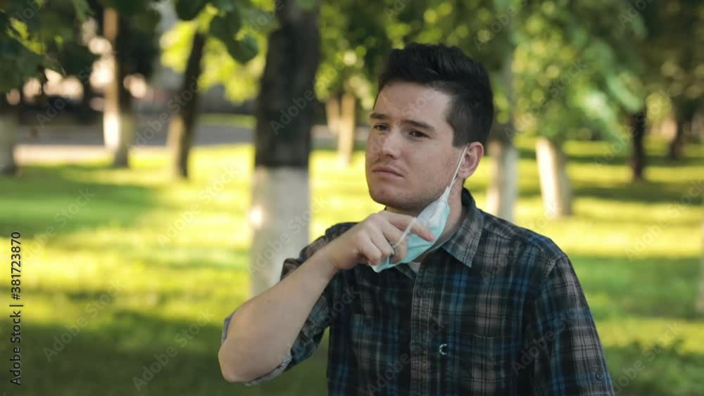 Breathing without mask. Young man stands in the city park, takes off the protective mask and starts breathing fresh air deeply. Boring and tired of pandemic and isolation Breathing without mask. Young man stands in the city park, takes off the protective mask and starts breathing fresh air deeply. Boring and tired of pandemic and isolation