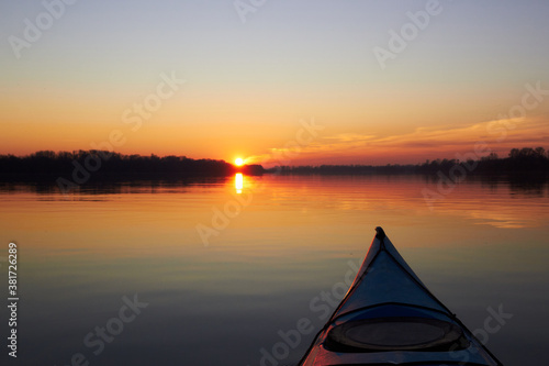 View from bow (prow) of blue kayak at colorful sunset over Danube river at autumn time