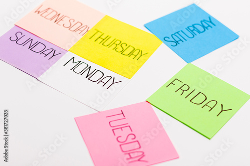 Sheets of paper in different colors are arranged in the shape of an arrow. Piece of paper has the name of one day of the week written on it.