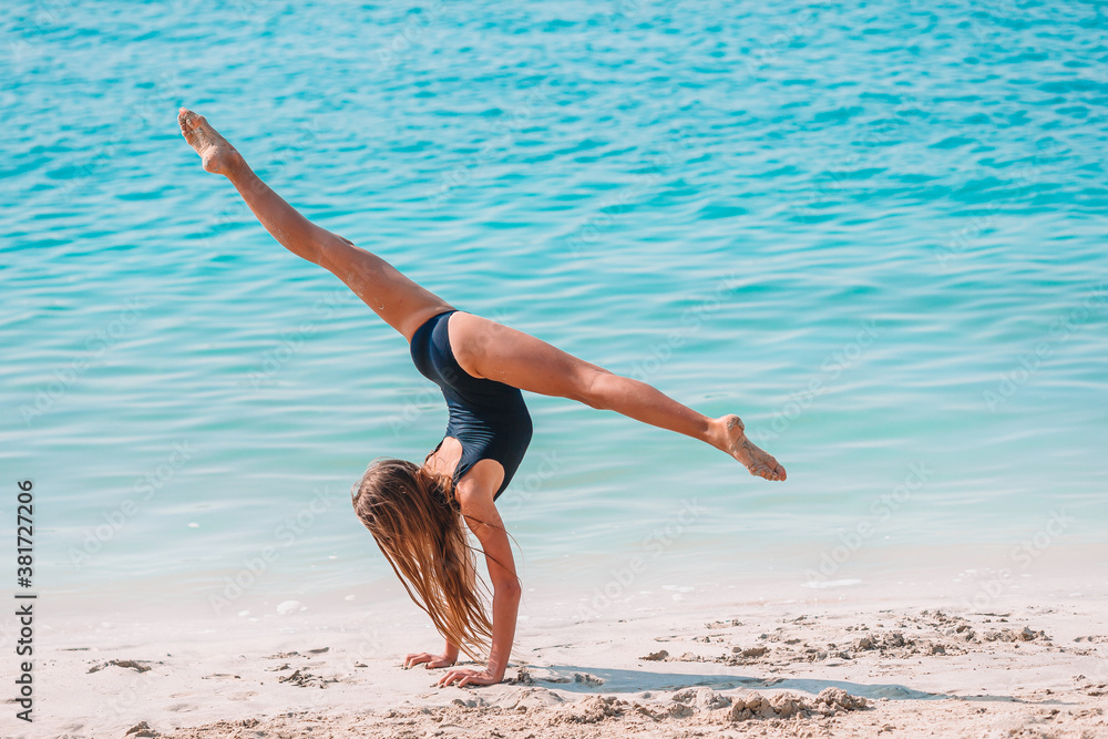 Active little girl at beach having a lot of fun. Cute kid making sporty exercises on the seashore Active little girl at beach having a lot of fun. Cute kid making sporty exercises on the seashore