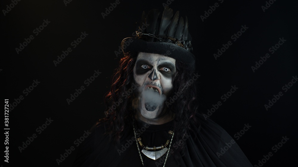 Sinister man with Halloween skeleton makeup exhaling cigarette smoking from his mouth and smiling