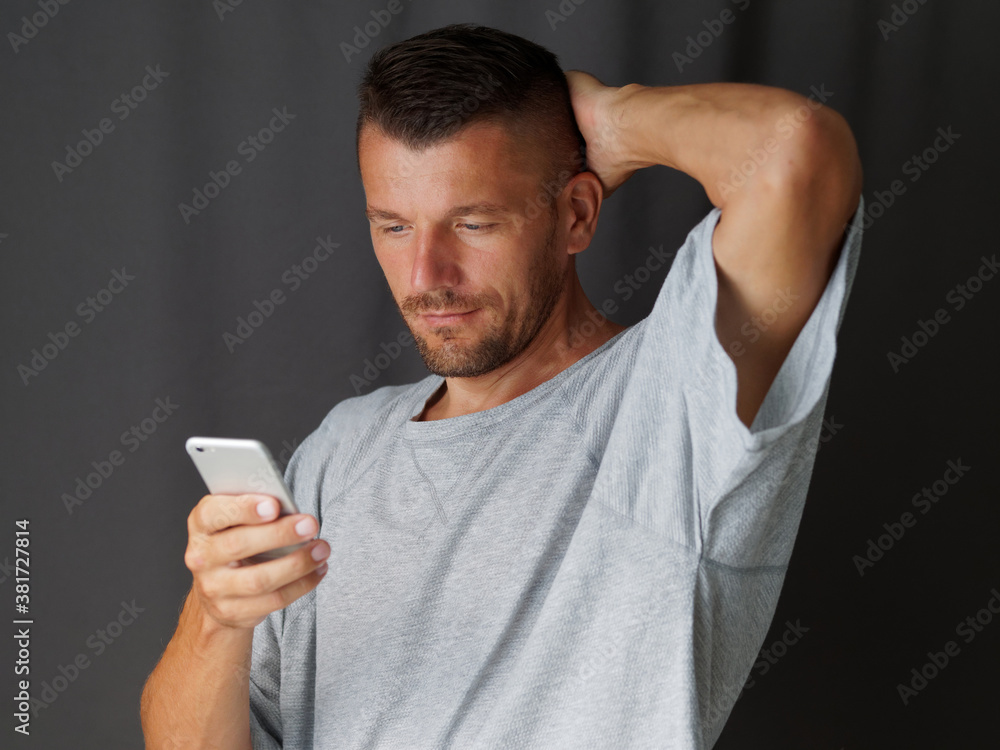Attractive man wears gray t-shirt using smartphone and smiling. Looking at smartphone. Attractive man wears gray t-shirt using smartphone and smiling. Looking at smartphone.