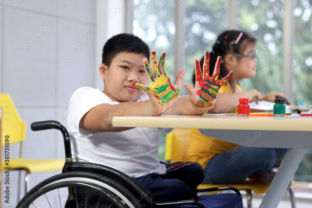 Disabled kids classroom, children having fun during study at school, kids learning together, schoolboy on wheelchair showing his painted hands Disabled kids classroom, children having fun during study at school, kids learning together, schoolboy on wheelchair showing his painted hands