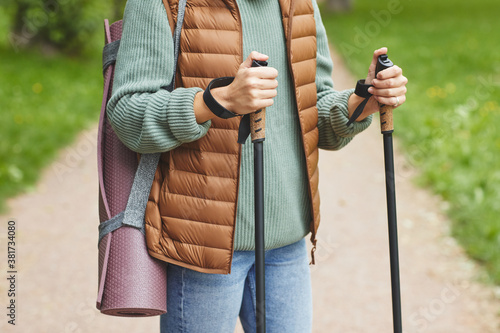 Close-up of man with exercise mat behind his back holding sticks and doing sport walking outdoors