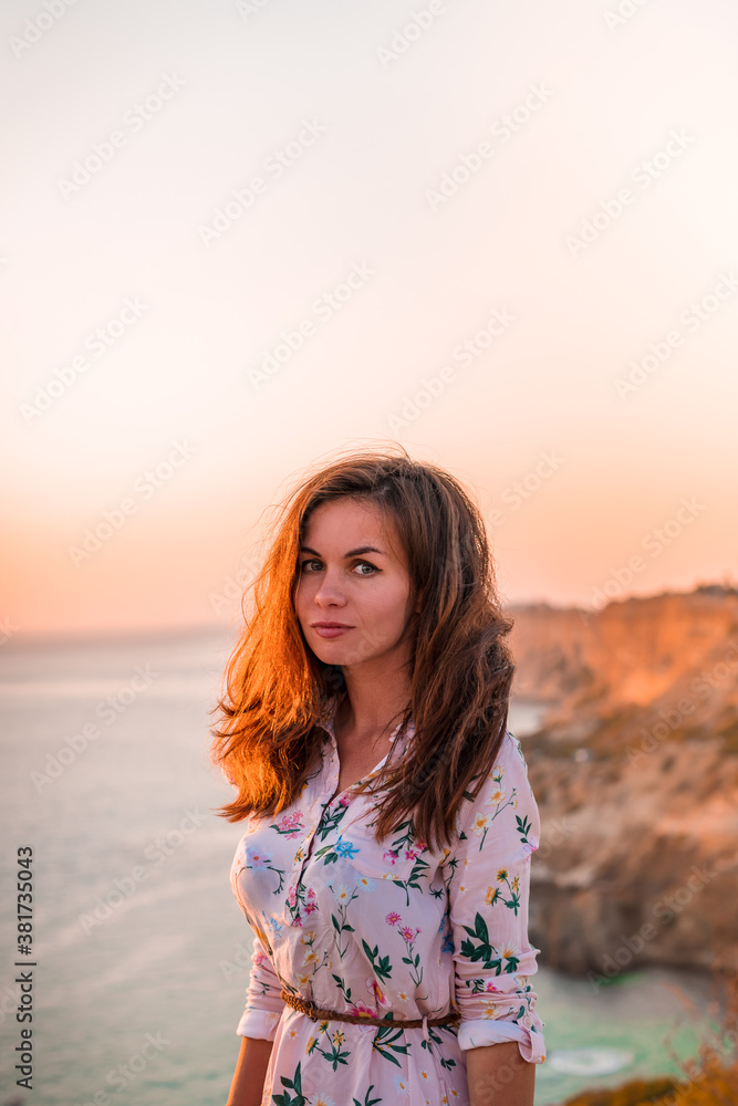 A young woman tourist stands on the shore high above the sea at sunset and admires Cape Fiolent in the Crimea A young woman tourist stands on the shore high above the sea at sunset and admires Cape Fiolent in the Crimea