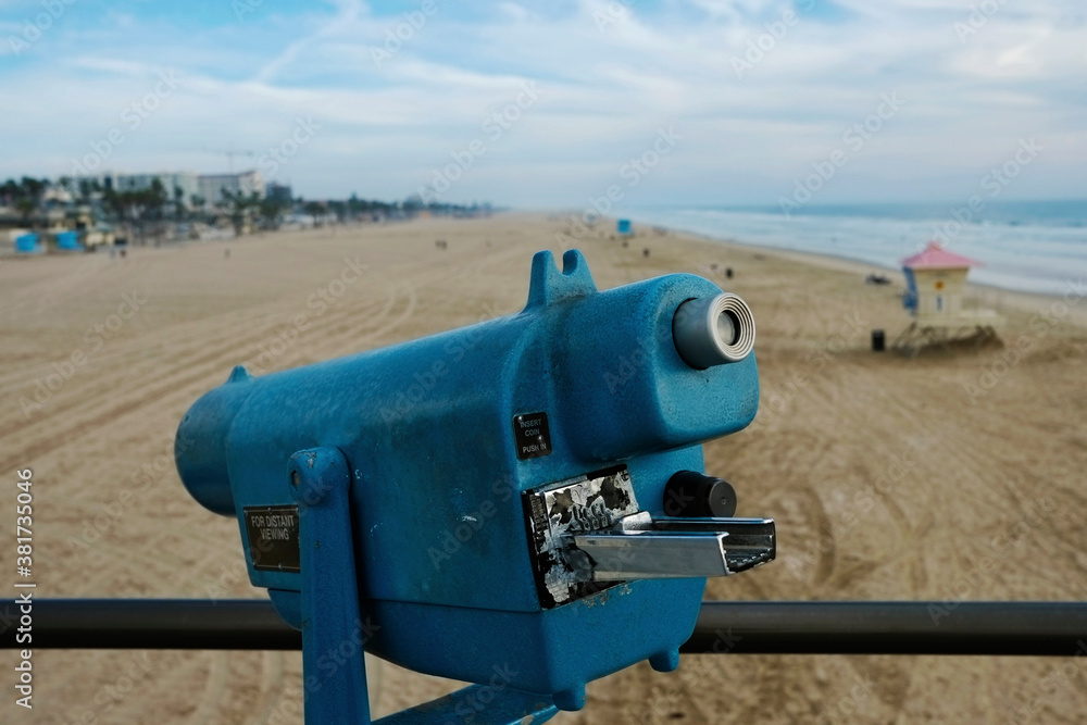 Binoculars telescope optics, tower viewer coin operated machine for touristic sightseeing beach. Lifeguard  house, Huntington Beach Pier, background, Orange County. Blue color, evening cloudy sky
