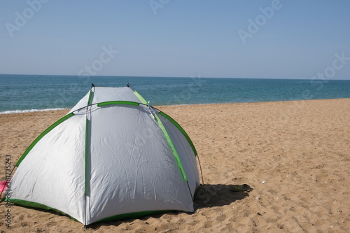 A lone green tourist tent stands on the seashore. 