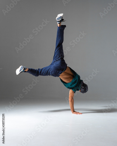 Cool b-boy dances on the floor standing on one hand isolated on gray background. Breakdance lessons photo