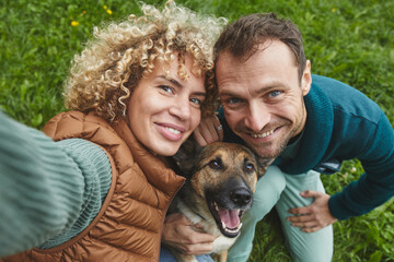 Portrait of young couple with dog smiling at camera while walking on the nature