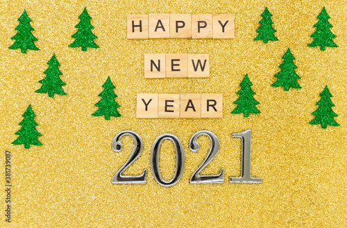 Words happy new year 2021 are written on wodden blocks on gold background with green christmas threes. Card. Banner. Metal numbers 2021