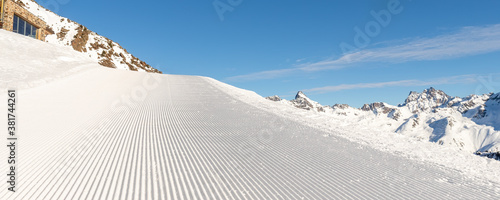 Obraz na plátně Close-up straight line rows of freshly prepared groomed ski slope piste with bright shining sun and clear blue sky background