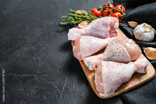 Raw chicken legs with spices and vegetables on a wooden cutting board. Black background. Top view. Copy space