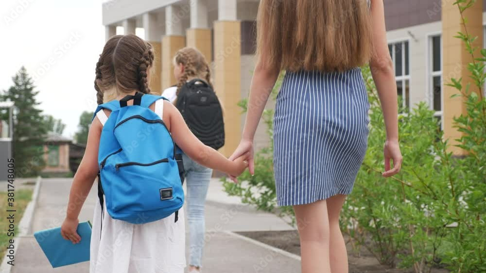 parent leads to school child with backpack back view. kids go to school with backpacks education concept. mom leads daughter by hand to first lesson. group school girl children lifestyle go to class