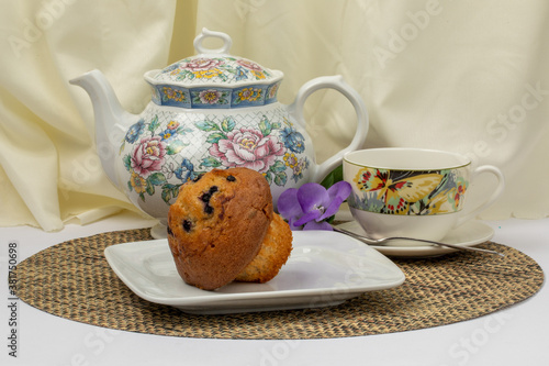 a blueberry muffin on a plate with a colorful teapot