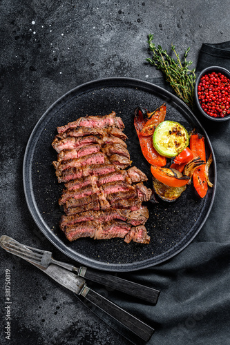 Sliced Chuck eye roll on a plate with a side dish of vegetables. Black background. Top view