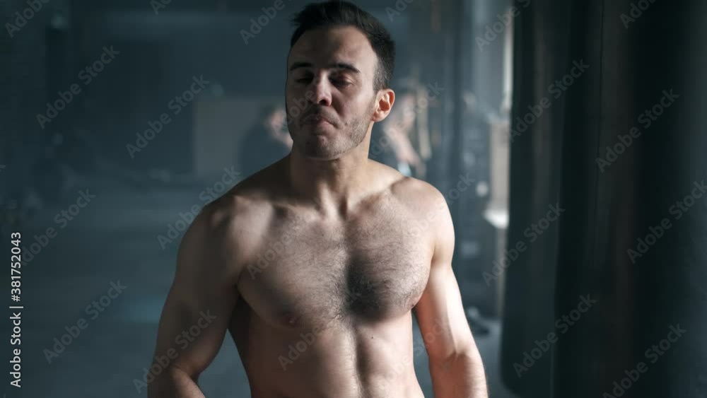 Attractive athletic shirtless young man drinking protein shake from shaker in gym and looking at camera and smiling Attractive athletic shirtless young man drinking protein shake from shaker in gym and looking at camera and smiling