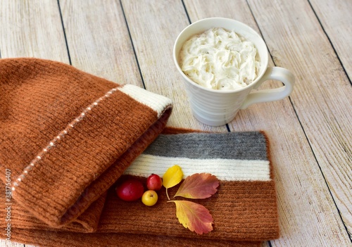 Warm mug of hot chocolate with seasonal wear of knit cap and scarf with background of autumn fall leaves 