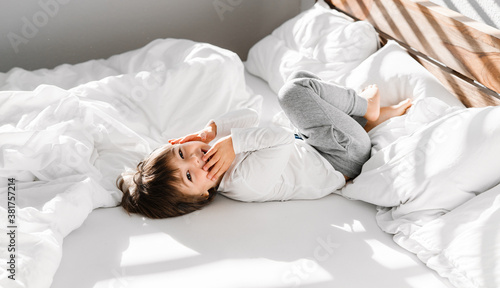 Cute little happy child boy playing in parents bed having fun at home at sunny morning. Light and shadows