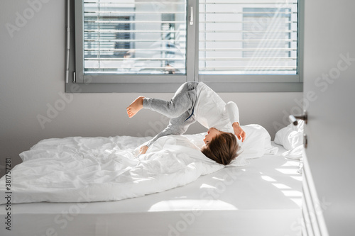 Quadro su tela Happy little child boy jumping on bed doing somersault having fun at home at sunny morning