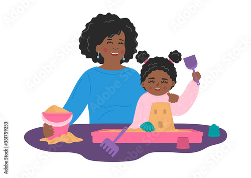 Mother with child plays with sand and toys in plastic sandbox on the table. African girl with nanny builds castle. Kids' sensory, motor skills, creativity and imagination development playing concept.