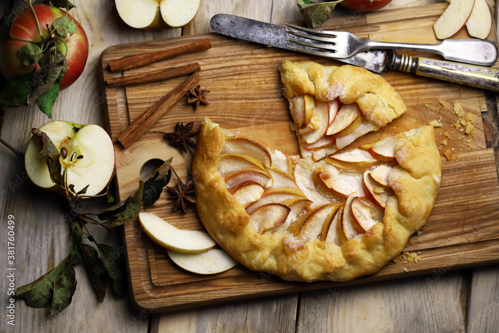 Homemade apple galette on a wooden board. Fresh apples with cinnamon leaves.