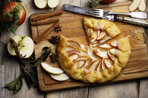 Homemade apple galette on a wooden board. Fresh apples with cinnamon leaves.
