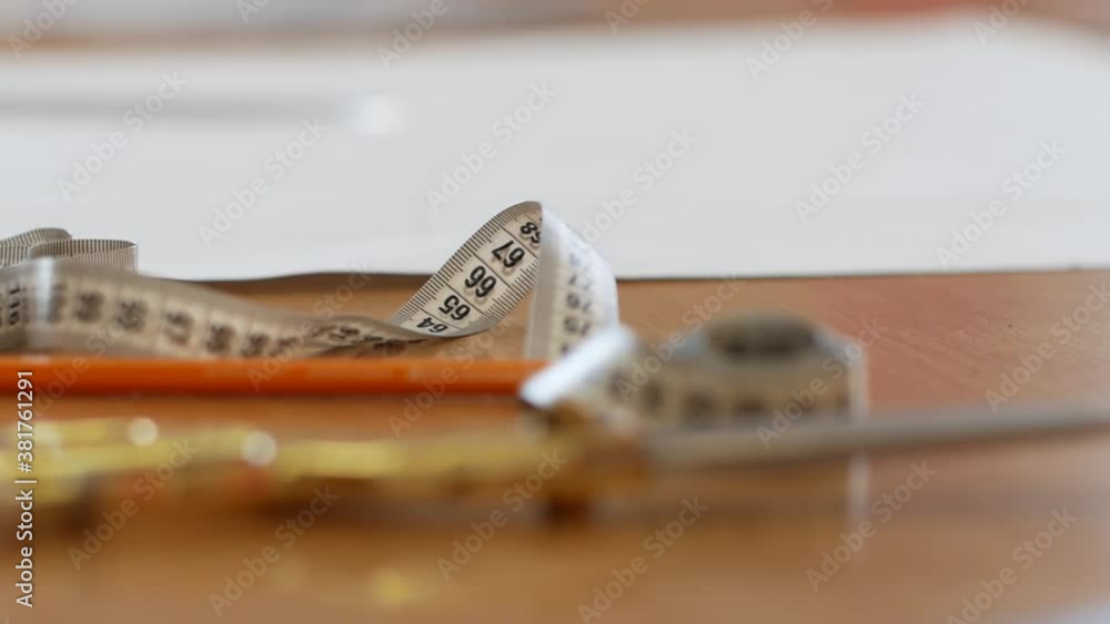A sewing measuring centimeter and scissors and pencil lie on the table of a textile factory. A sewing measuring centimeter and scissors and pencil lie on the table of a textile factory.