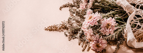 Beautiful bouquet of pink chrysanthemum flowers in a mesh bag on pale pink beige background. Trending minimalist horizontal banner with copy space for text.