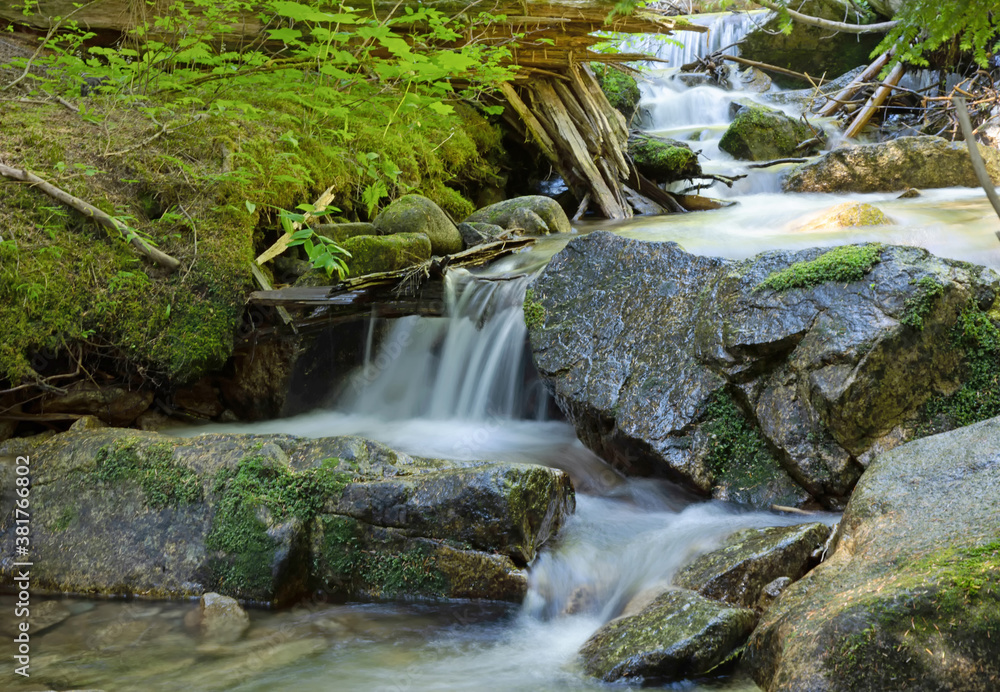 Fototapeta premium Original nature photograph of a small waterfall cascading over rocks with green foliage