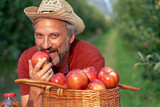Charismatic Mature Farmer with Hat Eating Red Apple in Sunny Orchard