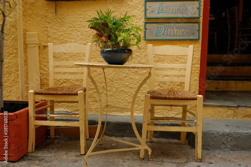 stolik i dwa krzesła przed drzwiami restauracji z napisem "lunch" i "dinner"w Grecji