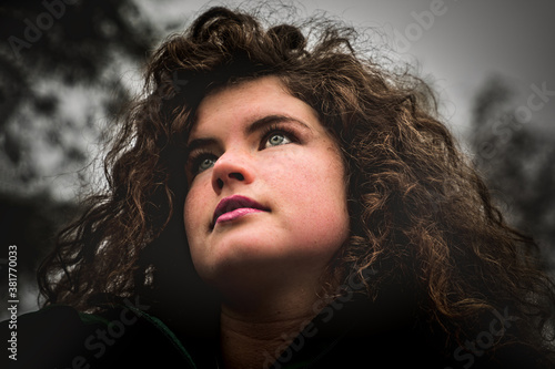 Young woman with wild curly hair looking hopefully in the distance