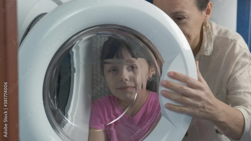 Mother with child by washing machine. A happy mother with her little daughter look through the door in the washing machine. Mother with child by washing machine. A happy mother with her little daughter look through the door in the washing machine.