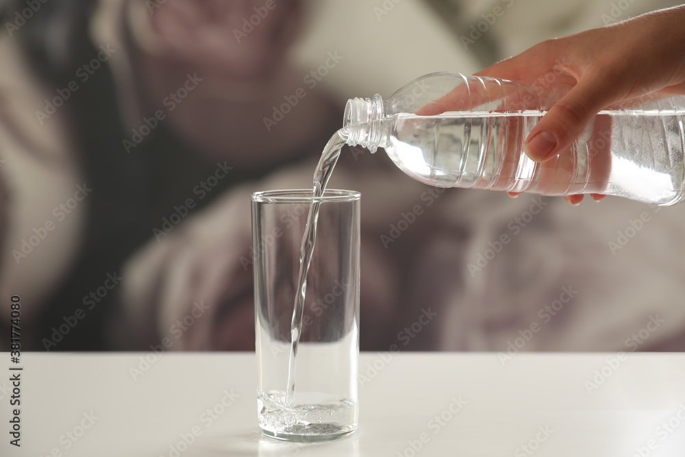 Woman pouring water from bottle into glass on table against blurred background, closeup
