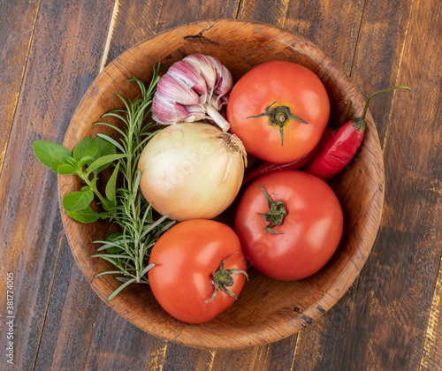 Tomatoes, garlic, peppers and herbs on a bowl over wood table