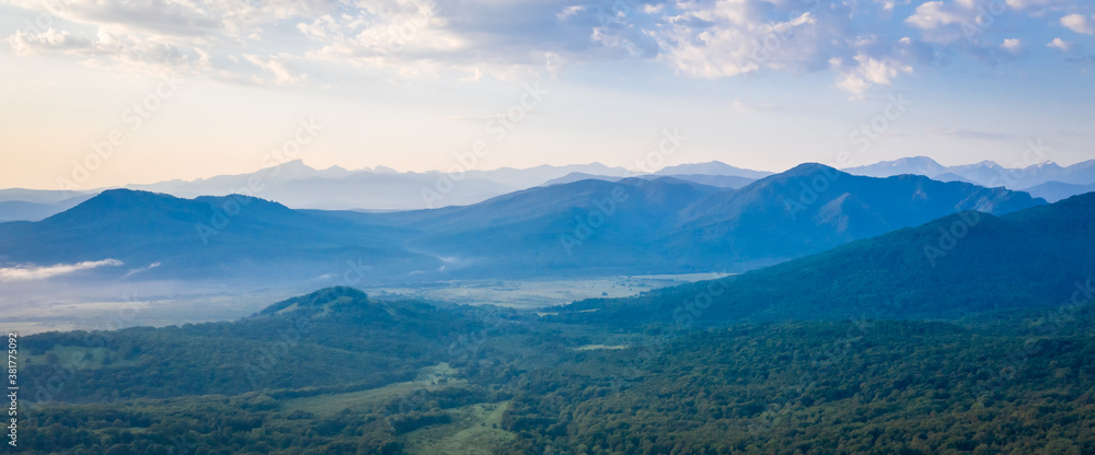 Early morning in the mountains. Morning sun and haze in the valley against the background of mountains. Mountain summer landscape. Banner size