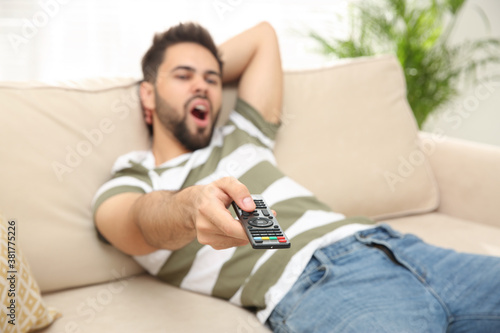 Lazy young man watching TV on sofa at home