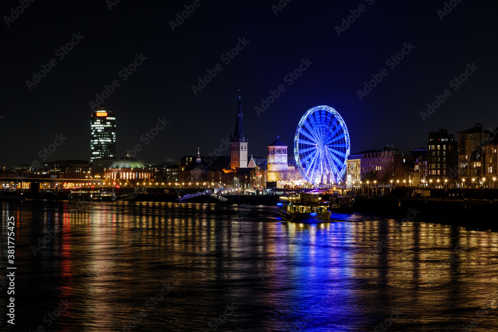 Night scenery on promenade and cityscape along riverside of Rhine river and background of Ferris wheel of Christmas market festival, Weihnachtsmarkt, in Düsseldorf, Germany.