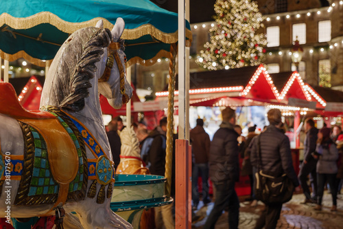 Selective focus at horse carousel and blur background of night illuminated atmosphere of Weihnachtsmarkt, Christmas market at Marktplatz around old town hall in Düsseldorf, Germany. 