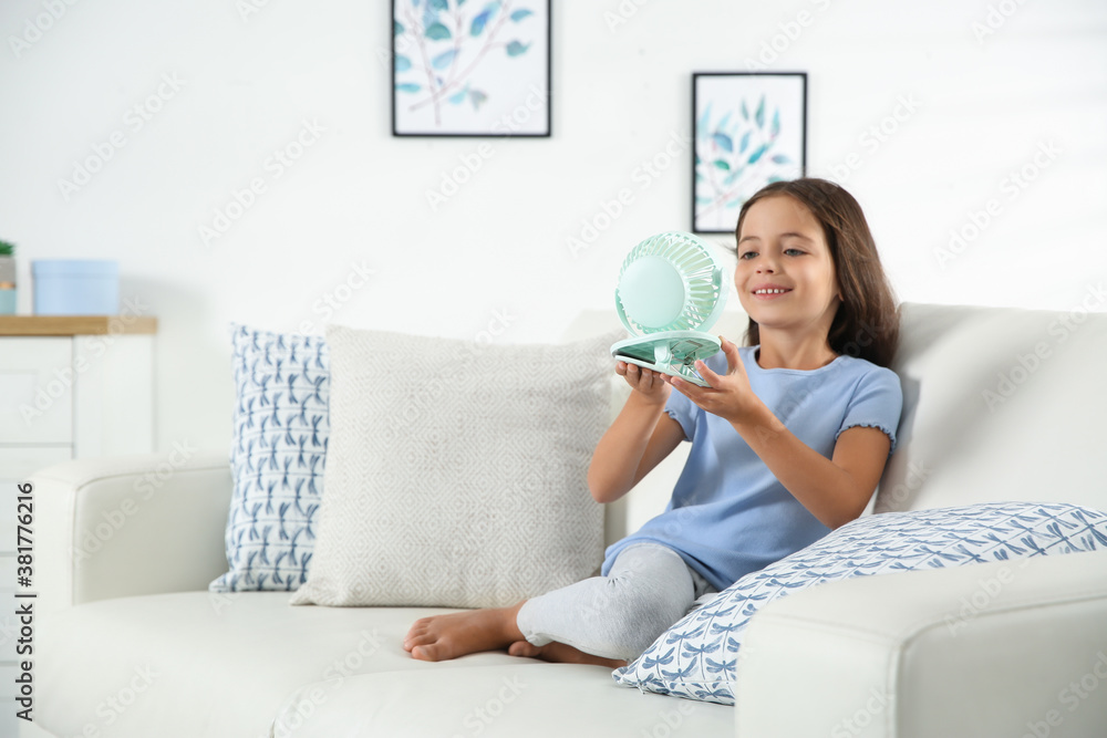 Little girl enjoying air flow from portable fan at home. Summer heat