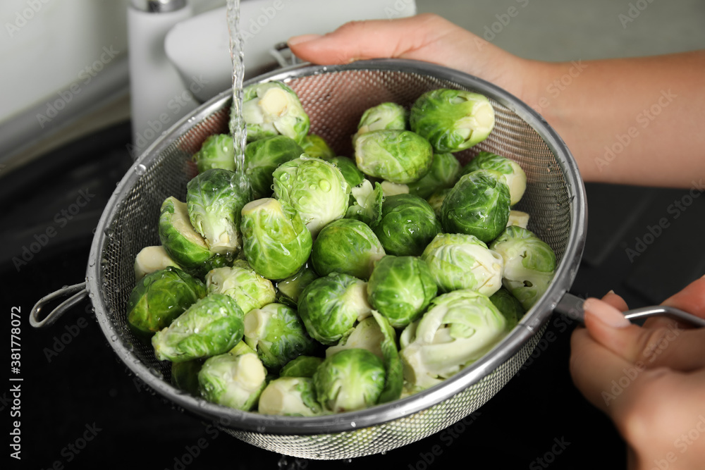 Woman washing Brussels sprouts with running water over sink, closeup Woman washing Brussels sprouts with running water over sink, closeup