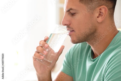 Man drinking pure water from glass indoors, closeup