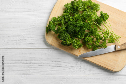 Fresh curly parsley, cutting board and knife on white wooden table, top view. Space for text