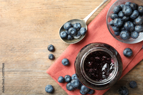 Jar of blueberry jam and fresh berries on wooden table, top view. Space for text