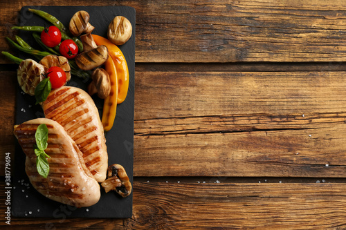 Tasty grilled chicken fillets with vegetables on wooden table, flat lay. Space for text