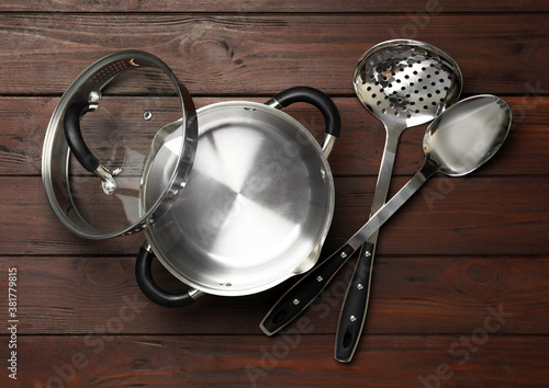 Modern saucepan, skimmer and spoon on brown wooden table. Cooking utensils